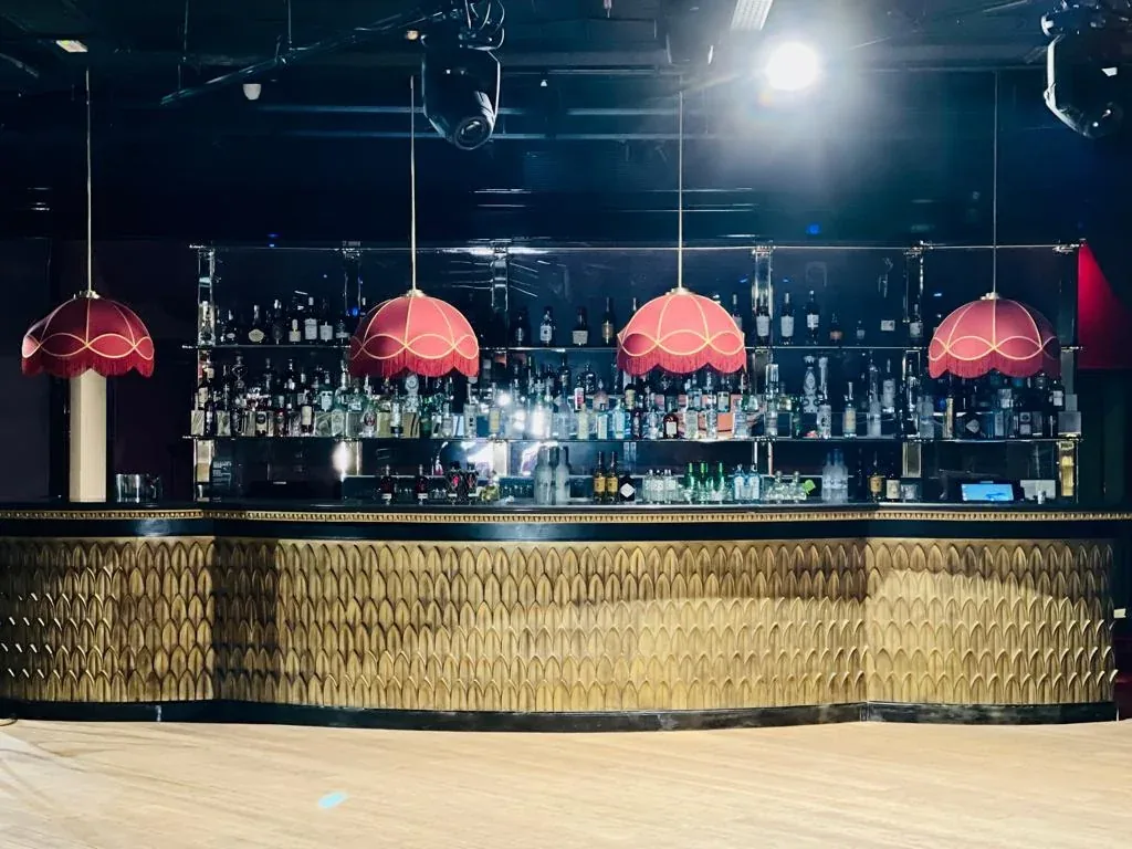 Barra de Club Chinois con frente dorado, botellas al fondo y cuatro lámparas rojas.