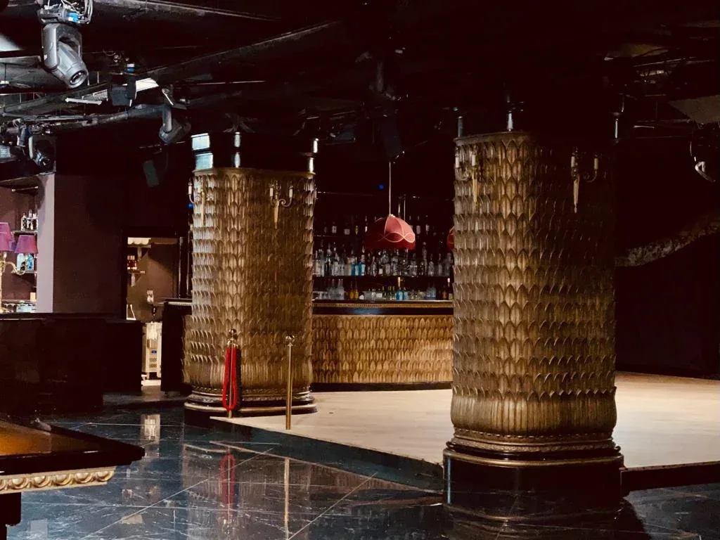 Columnas decoradas de acabado dorado en Club Chinois, con una barra al fondo y pavimento oscuro.