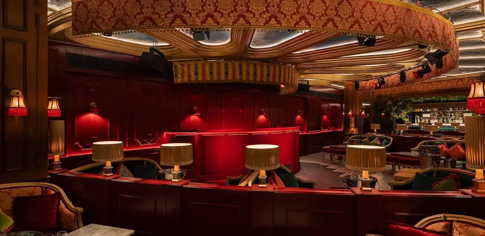 Salón de Club Chinois con asientos rojos, lámparas de mesa y techo curvo con detalles dorados.