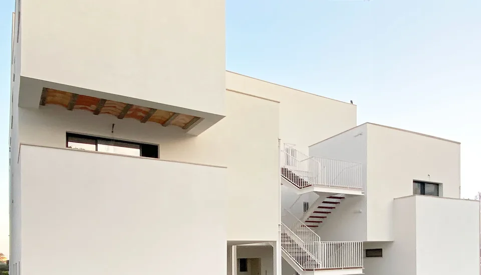 Fachada de Colonia Sant Jordi con volúmenes blancos, balcones y una escalera exterior.