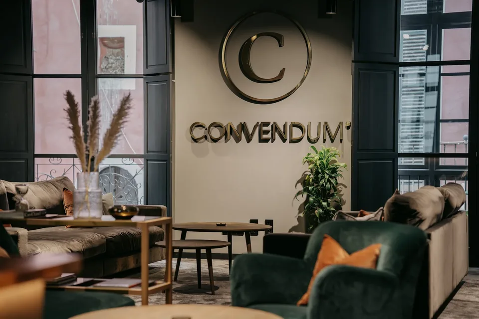 Logotipo de CONVENDUM Palma en la pared de una zona de estar con sofá, sillón verde y mesas bajas.