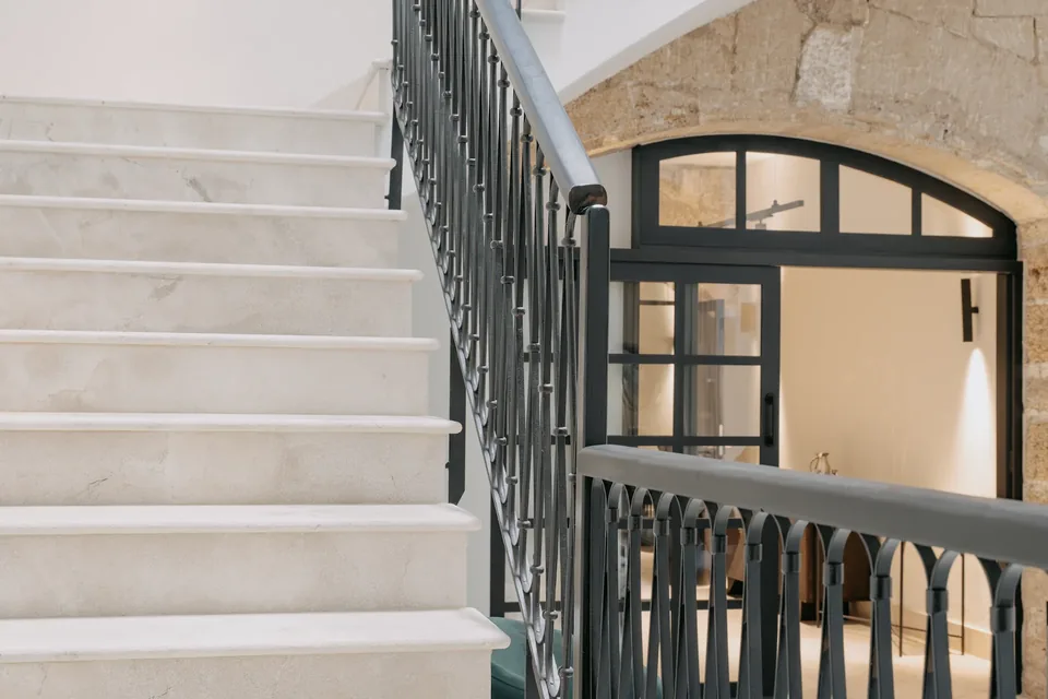 Detalle de la escalera y barandilla de CONVENDUM Palma, con un arco y una puerta acristalada al fondo.