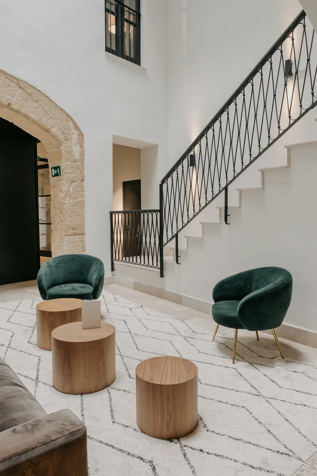 Zona de estar de CONVENDUM Palma con sillones verdes, mesas bajas y una escalera en el espacio de doble altura.