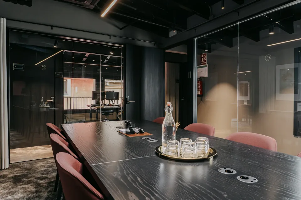 Sala de reuniones de CONVENDUM Palma con mesa alargada, sillas rojizas y cerramiento acristalado.
