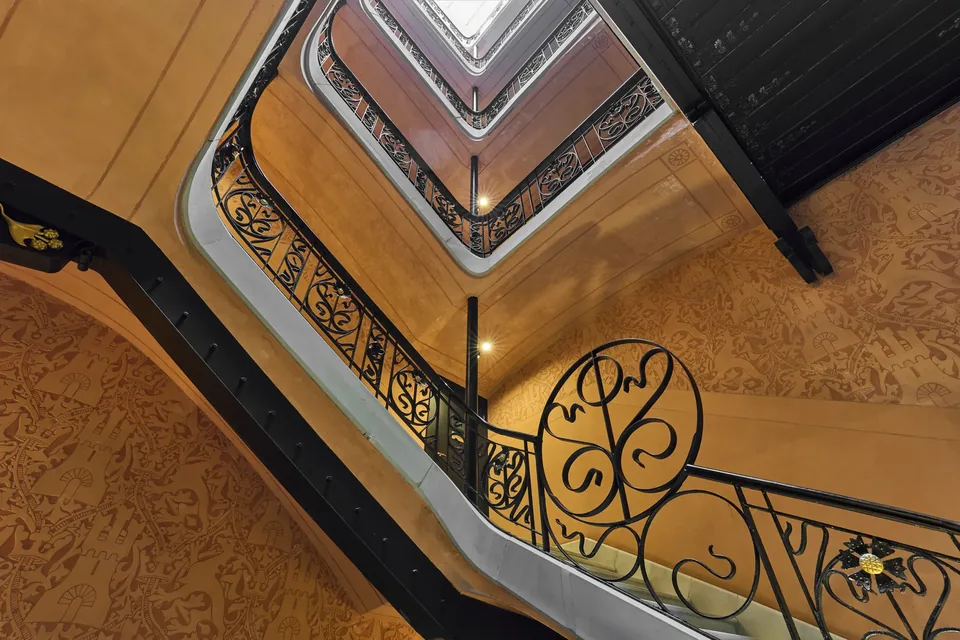 Vista ascendente de la escalera del Hotel España Ocean Drive con barandillas oscuras, paredes cálidas y luz cenital.