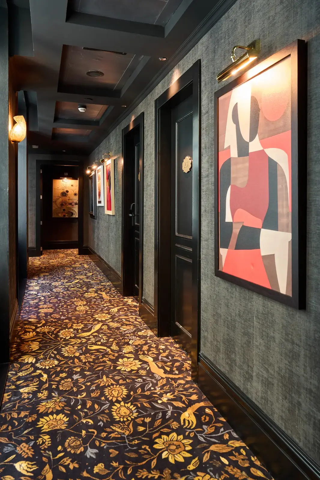 Pasillo del Hotel España Ocean Drive con puertas oscuras, cuadros y una alfombra de motivos multicolores.