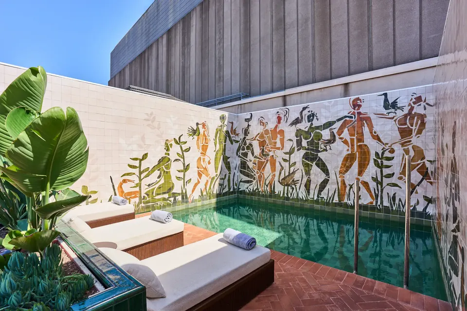 Piscina del Hotel España Ocean Drive con tumbonas, vegetación y un mural sobre las paredes que rodean el agua.