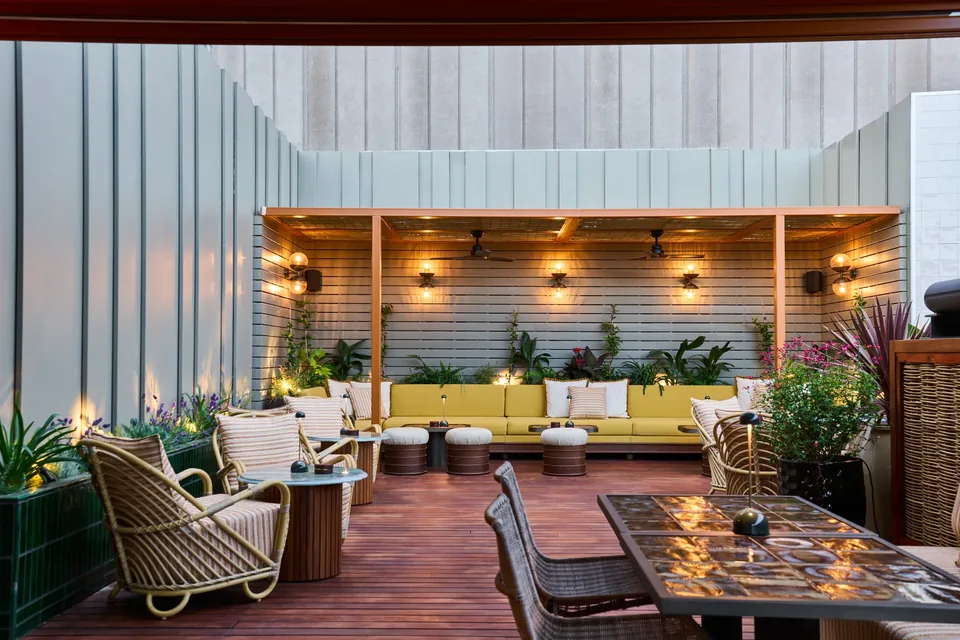 Terraza del Hotel España Ocean Drive con sillones, sofá amarillo y una pérgola junto a paredes de paneles verticales.