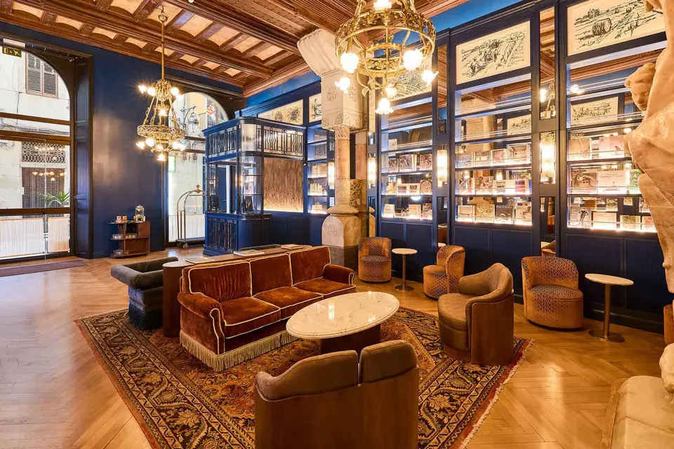 Vestíbulo del Hotel España Ocean Drive con sofás y sillones junto a vitrinas azules, columnas y puertas acristaladas.