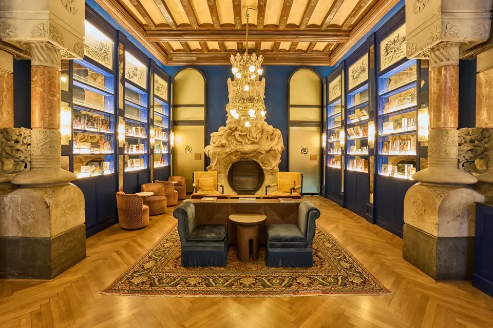 Vestíbulo del Hotel España Ocean Drive con columnas, vitrinas azules, techo de vigas y una chimenea al fondo.