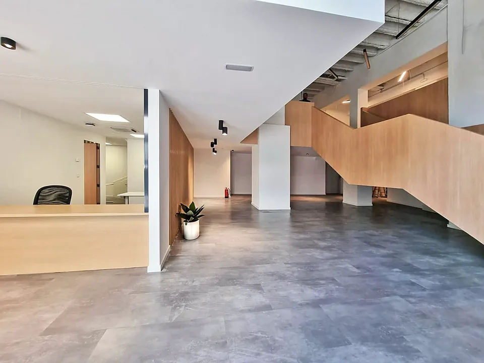 Zona de acceso de ILERNA Barcelona con mostrador, escalera de laterales claros y una planta junto al pilar.