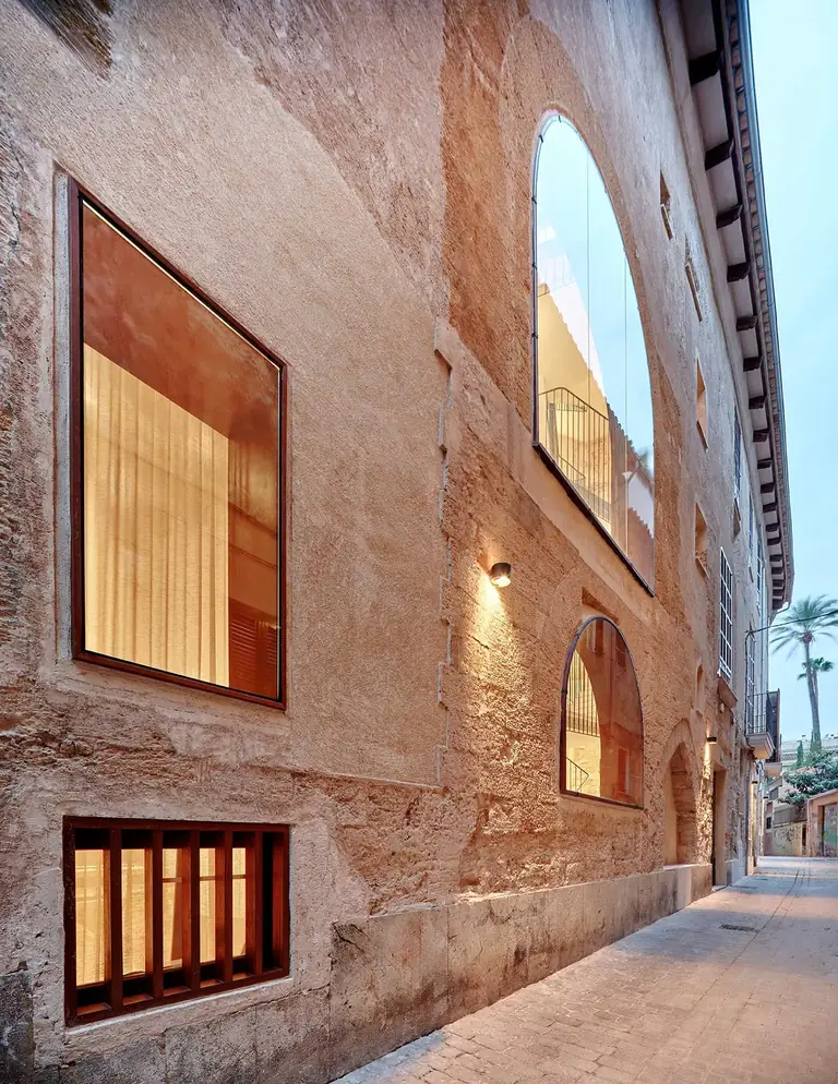 Fachada de Nobis Hotel Palma junto a una calle estrecha, con ventanas iluminadas y un gran arco superior.