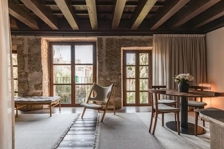 Zona de estar de Nobis Hotel Palma con sillones, mesa y cortinas junto a dos ventanas bajo un techo de vigas.