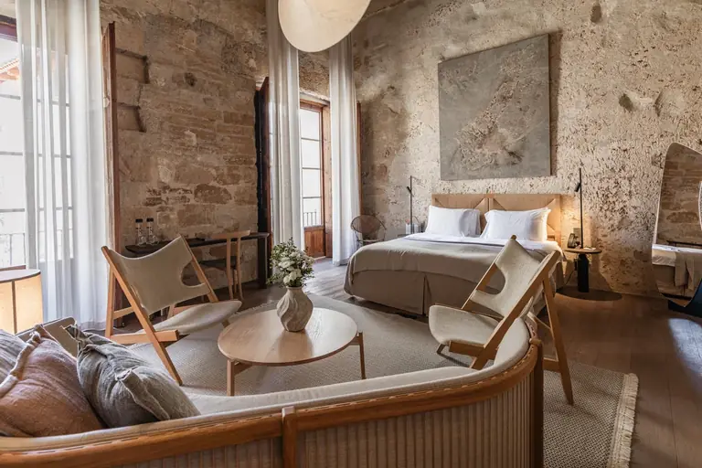 Habitación de Nobis Hotel Palma con cama, sillones y mesa baja junto a grandes ventanales con cortinas.