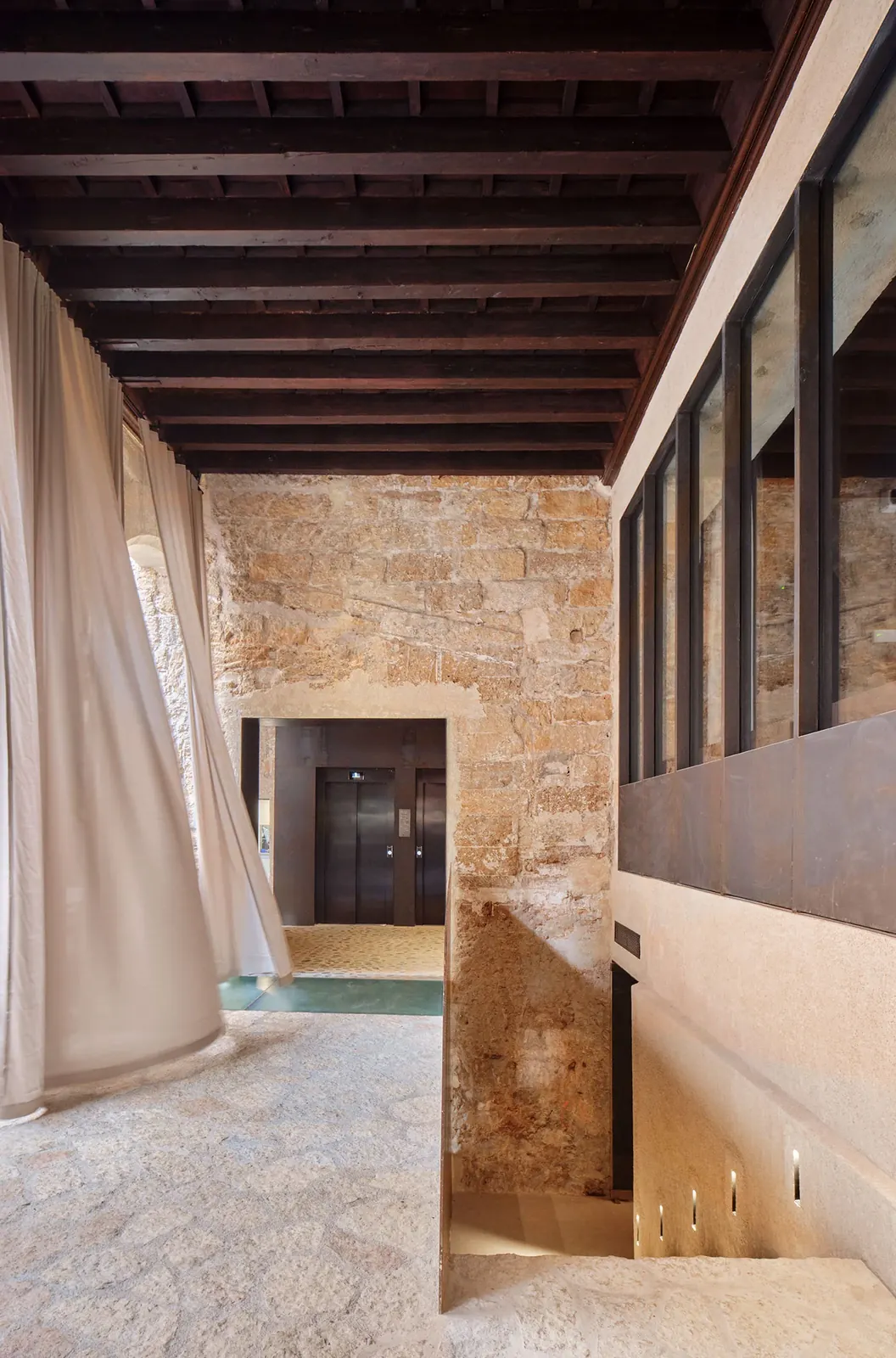 Pasillo de Nobis Hotel Palma con techo de vigas, cortinas claras y una escalera tras un cerramiento acristalado.