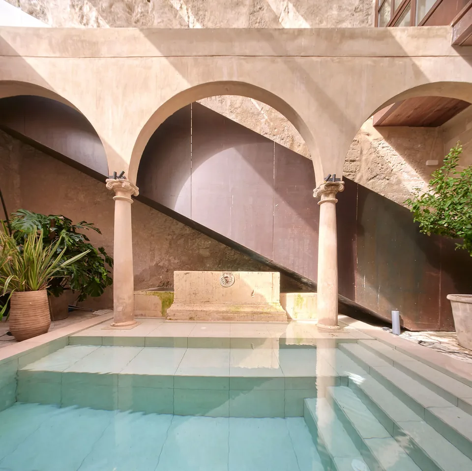 Piscina de Nobis Hotel Palma junto a columnas, arcos y una escalera lateral iluminados por el sol.
