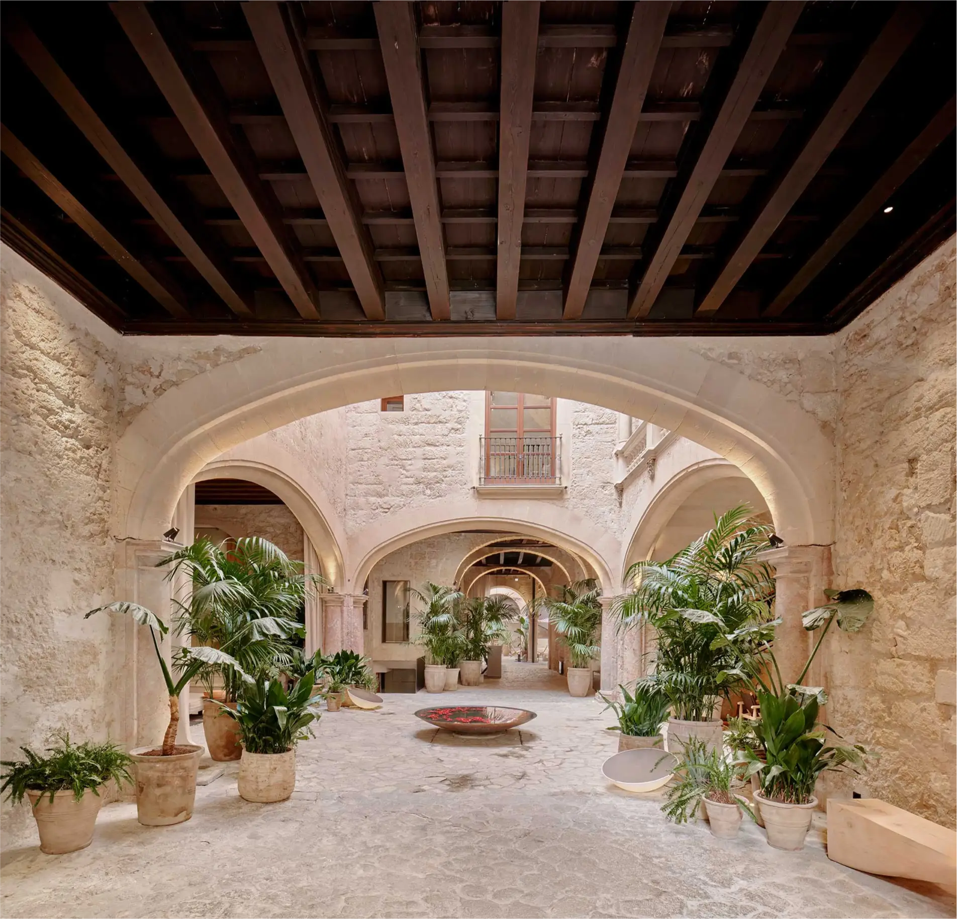 Patio de Nobis Hotel Palma con arcos de piedra, techo de madera y vegetación.