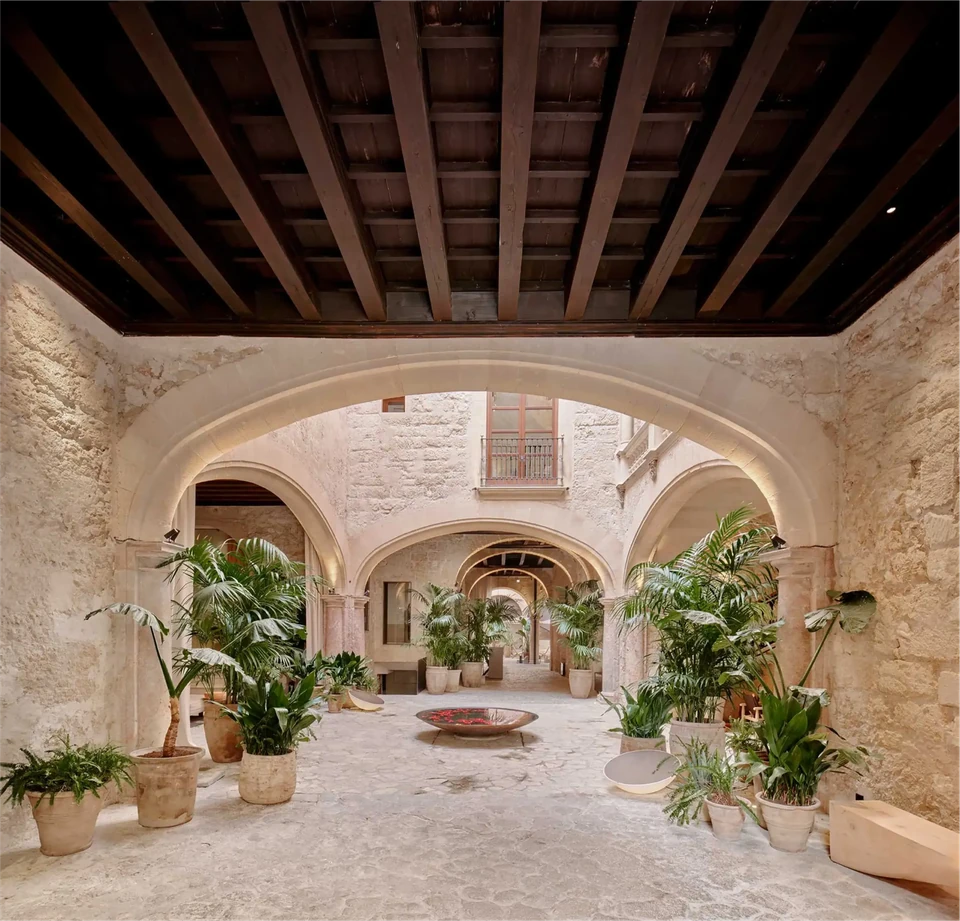 Patio de Nobis Hotel Palma con arcos de piedra, techo de madera y vegetación.