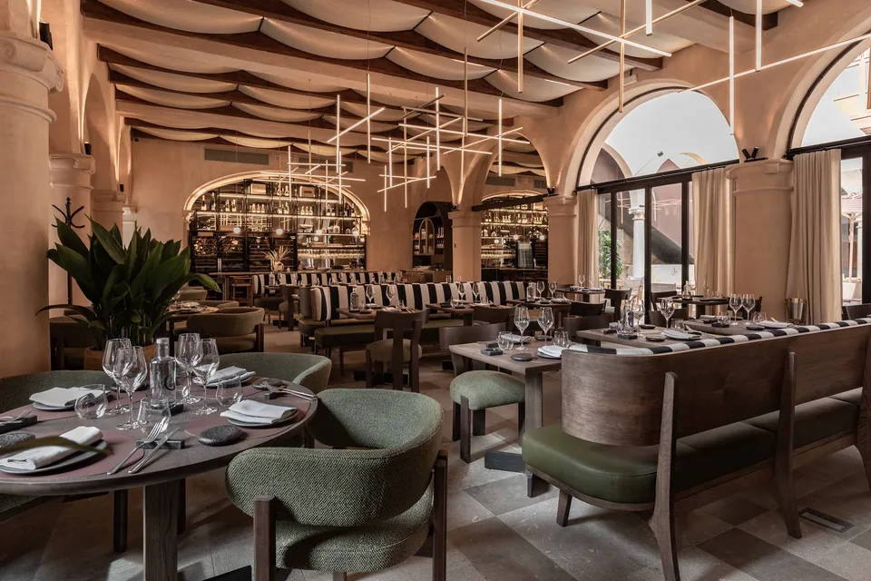 Restaurante de Nobis Hotel Palma con mesas redondas, sillas verdes y grandes ventanales con arcos.