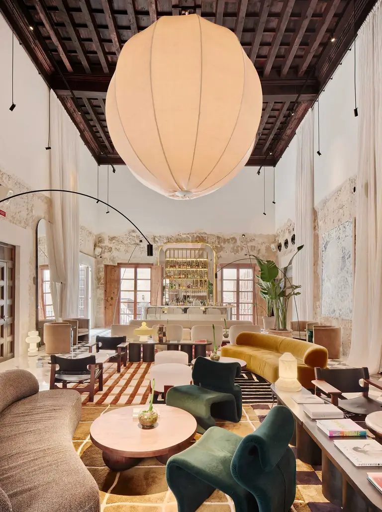 Salón de Nobis Hotel Palma con sofás de varios colores y una gran lámpara clara bajo un techo de vigas.