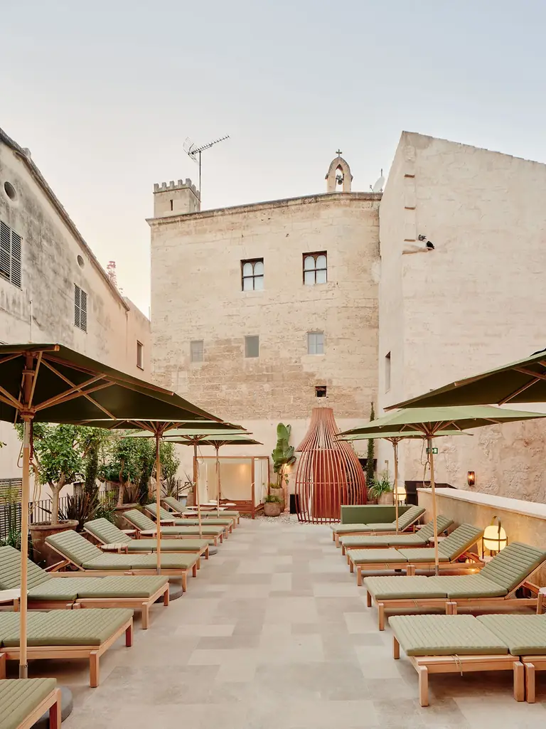Terraza de Nobis Hotel Palma con tumbonas, sombrillas y edificios claros alrededor.