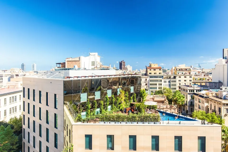 Vista elevada de Ocean Drive Barcelona con fachada clara, un volumen acristalado y una terraza con vegetación y piscina.