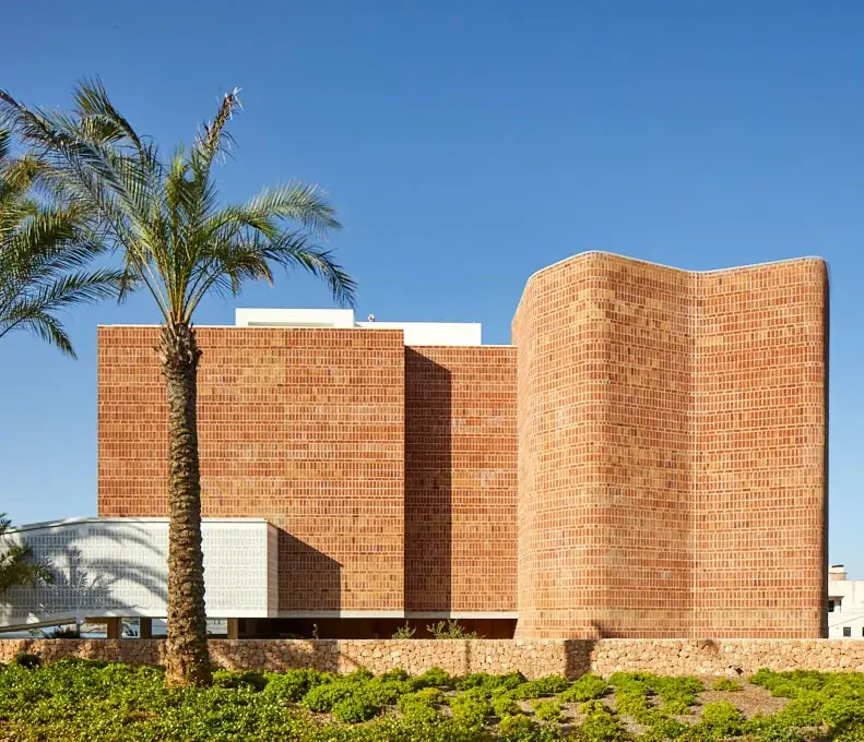Exterior de Ocean Drive Talamanca con volúmenes de ladrillo visto, una palmera y vegetación baja.