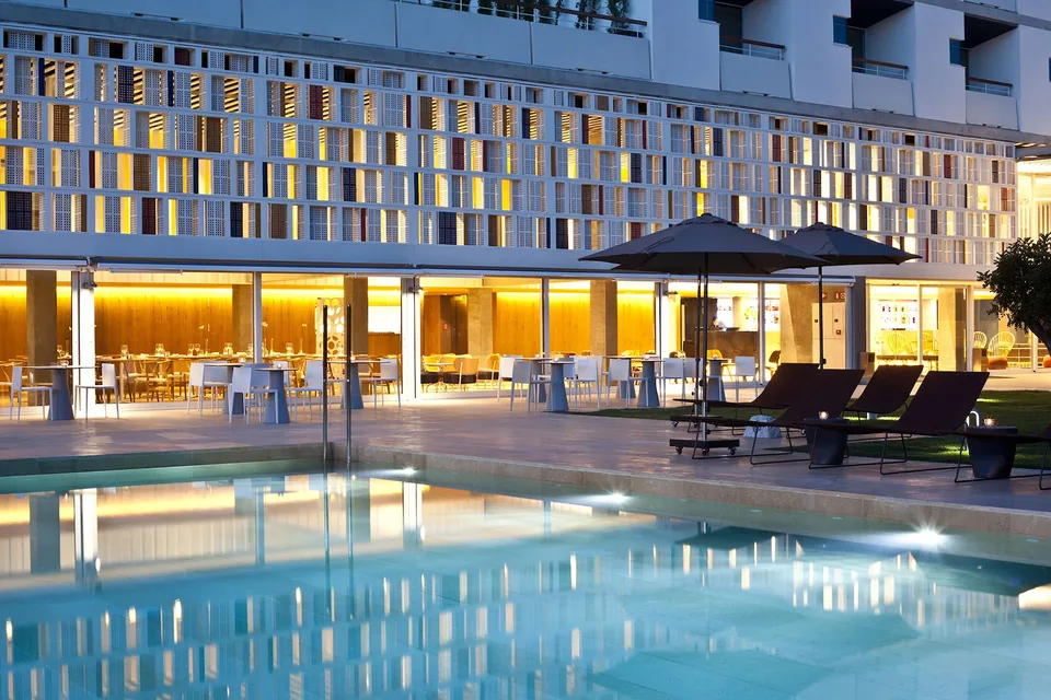 Fachada de OD Port Portals con iluminación cálida, piscina y tumbonas al anochecer.