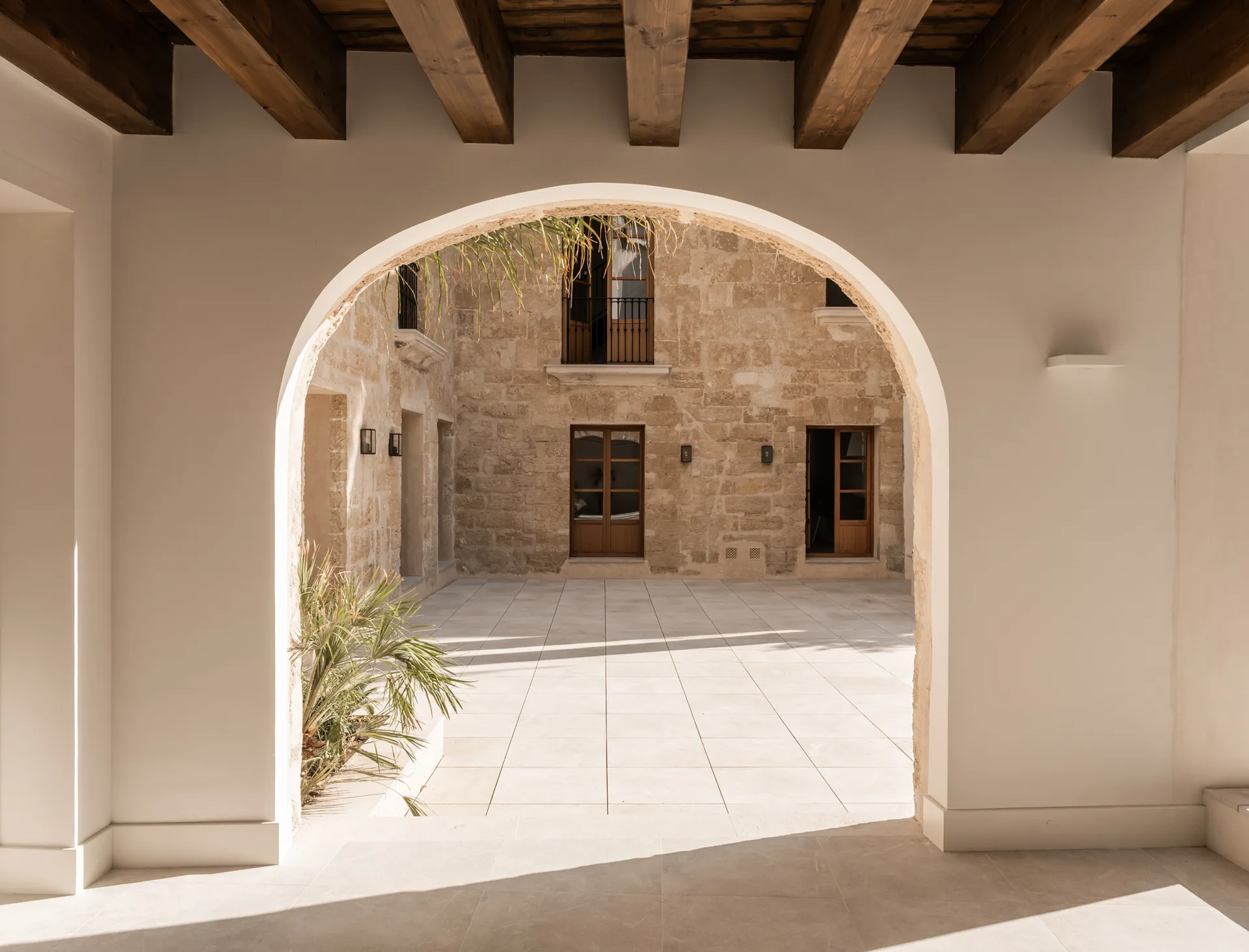 Vista del patio de Residencia histórica en Palma a través de un arco, con vigas de techo y pavimento claro.