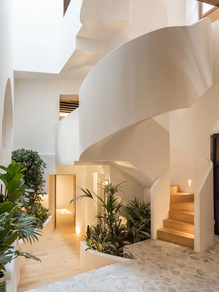 Escalera curva de la Carrer Sol en Palma con laterales blancos, peldaños de tono madera y plantas junto al distribuidor.