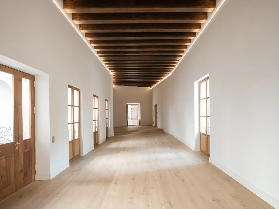 Sala de la Carrer Sol en Palma con pavimento de tono madera, puertas acristaladas y un techo de vigas iluminado.